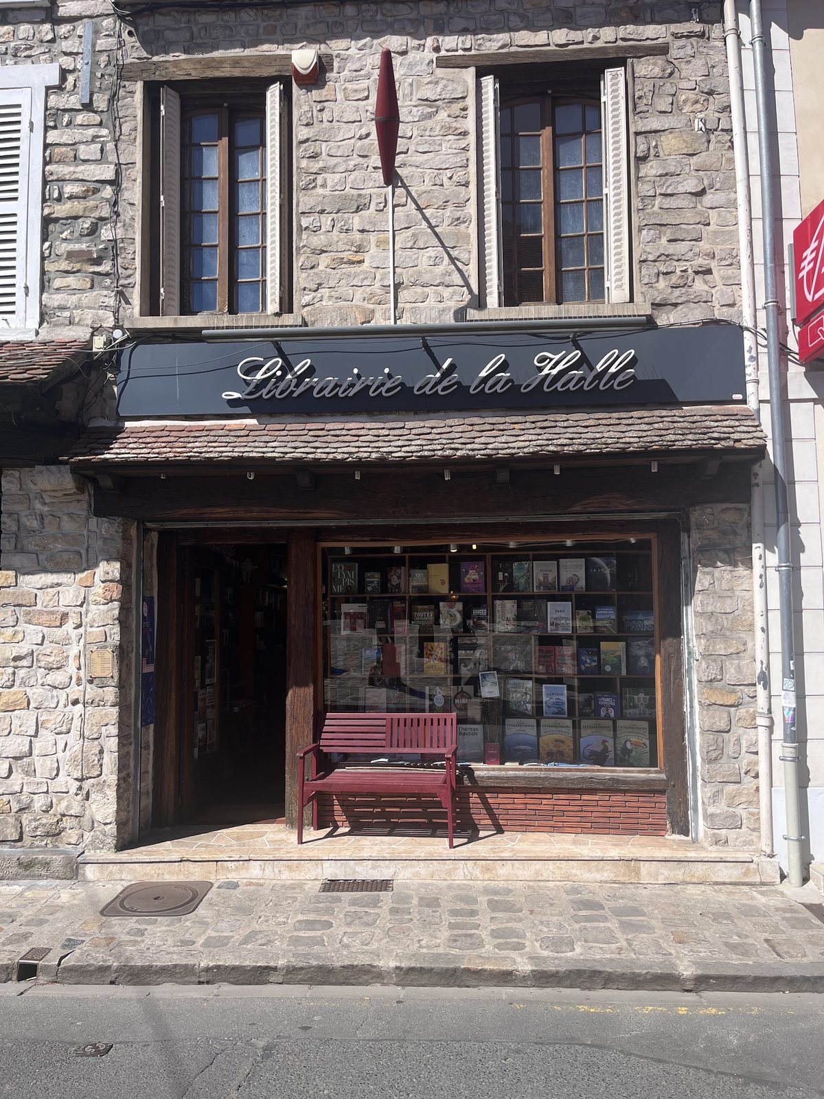 La façade en pierre de la Librairie de la Halle, enseigne en bois et vitrine de livres